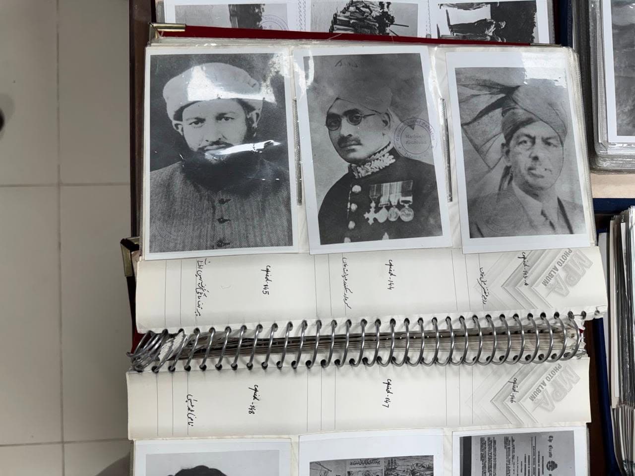 An open album page with three black-and-white portrait photographs above handwritten Urdu labels