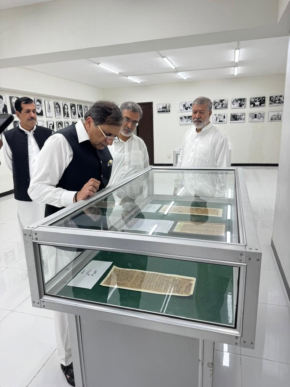 A visitor studying old handwritten documents in a glass showcase, with black-and-white photographs lining the walls