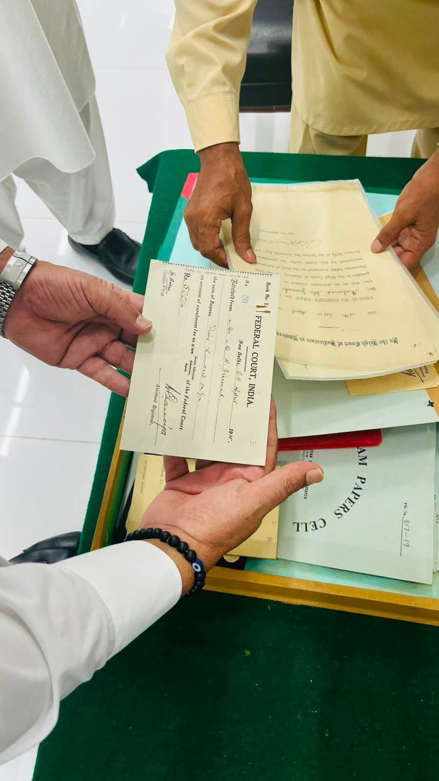Hands holding a Federal Court of India enrolment fee receipt above a tray of papers from the Quaid-e-Azam Papers Cell