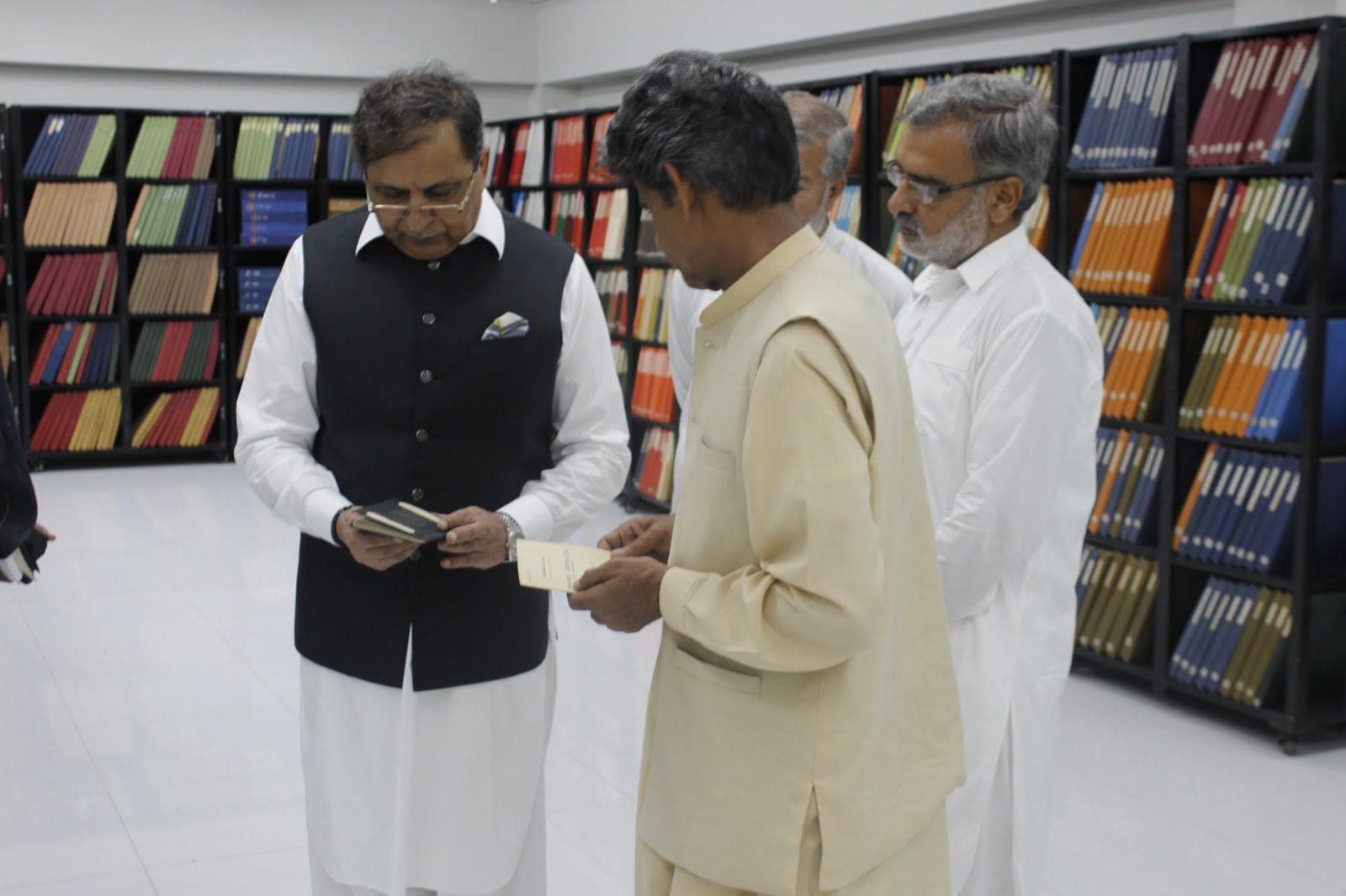 Visitors examining small documents in a room lined with shelves of coloured file boxes