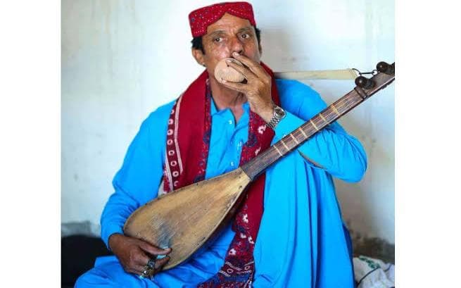 A musician playing the boreendo, the small clay folk flute, with a stringed instrument in his lap