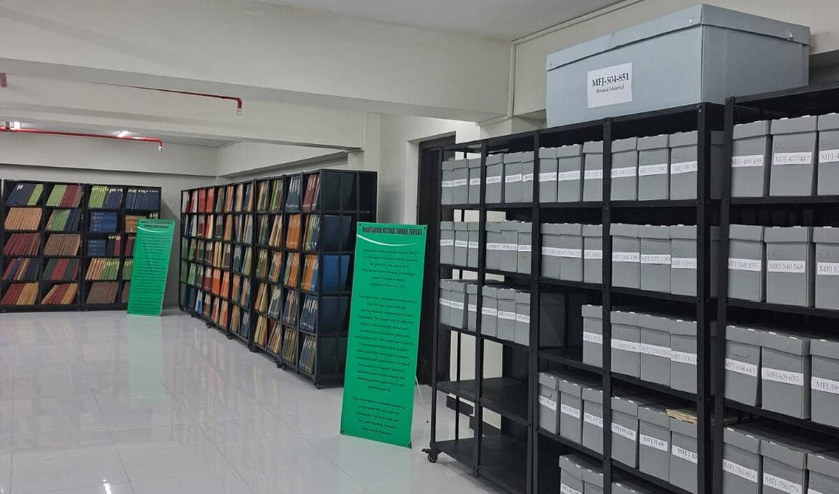 Shelves of labelled archive boxes and bound volumes at the National Archives of Pakistan, with display boards for the Mohtarma Fatima Jinnah Papers