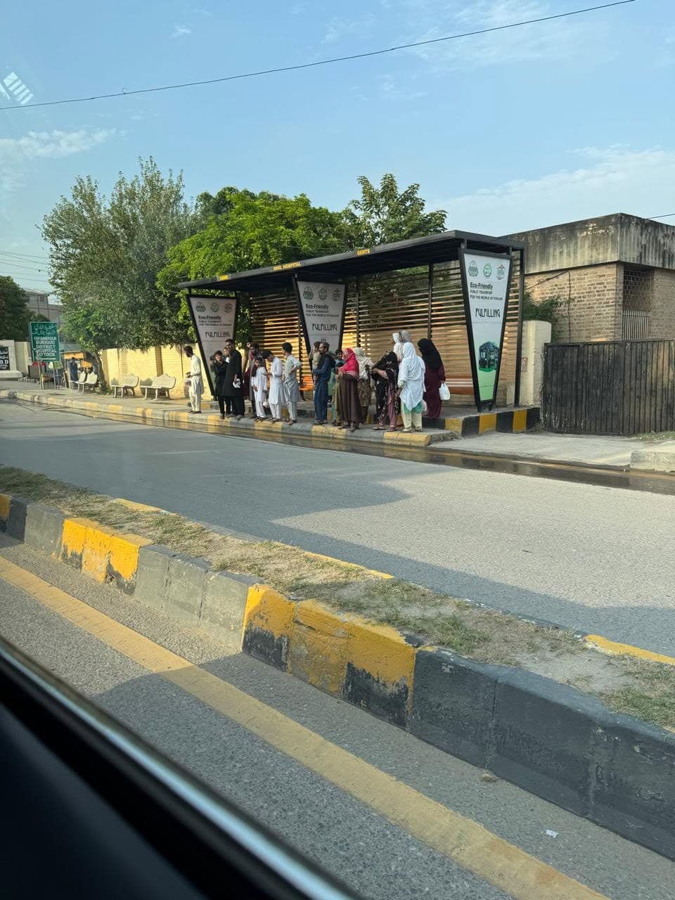 People waiting at a modern roadside bus shelter with eco-friendly public transport signs
