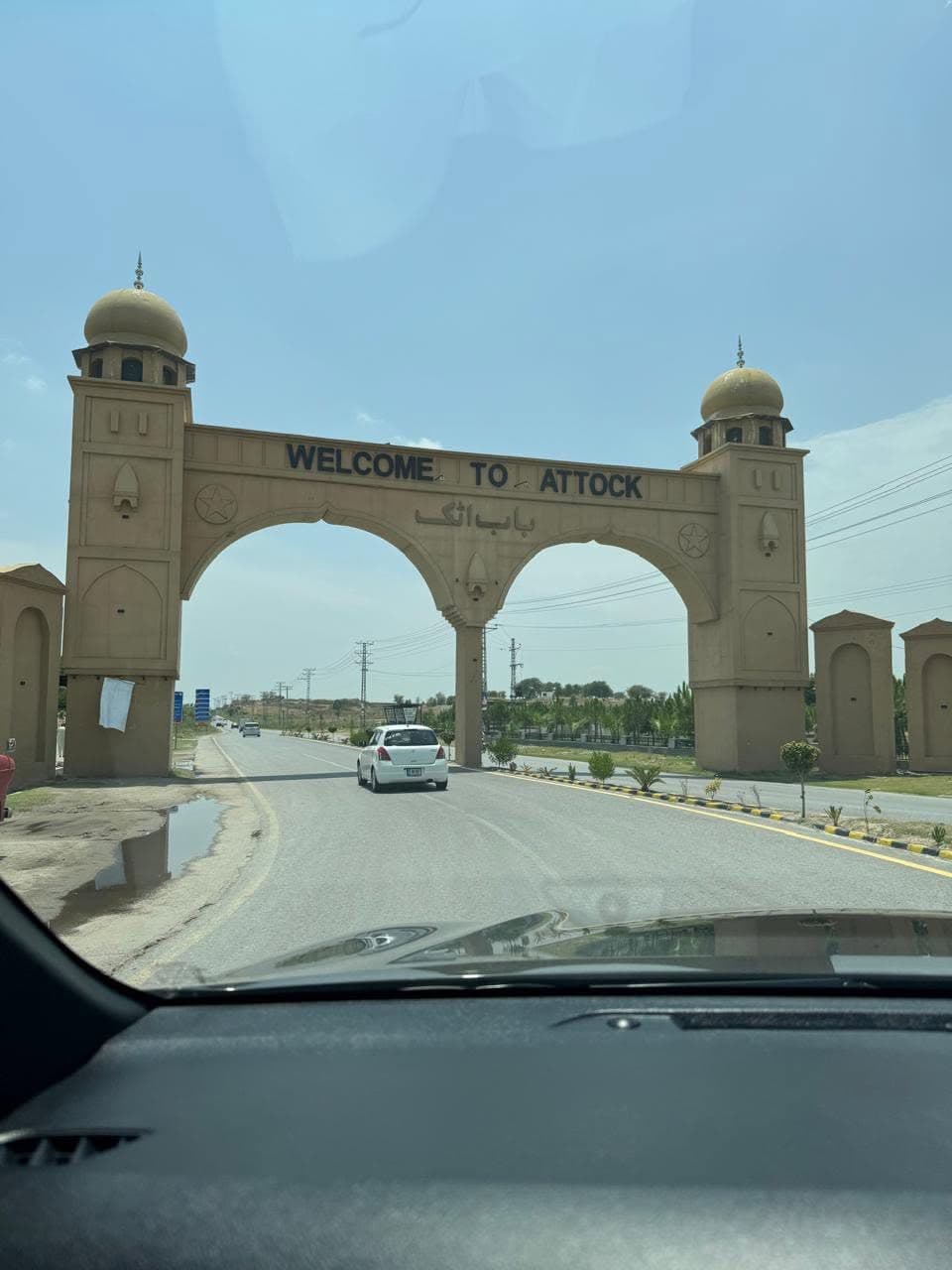 A domed double-arched gateway reading Welcome to Attock, seen through a car windscreen