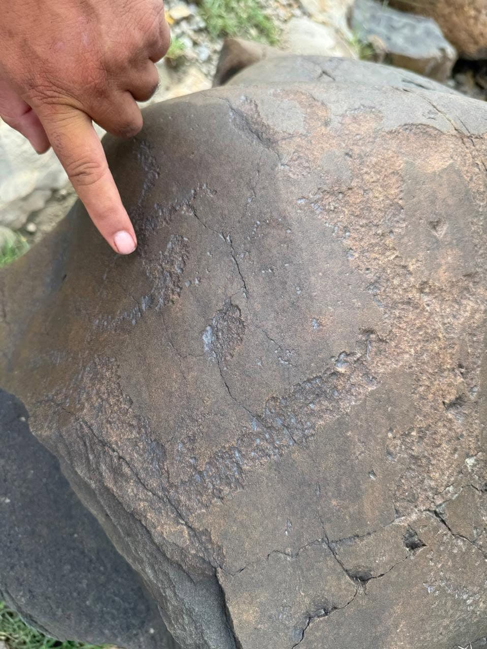 A finger pointing to faint pecked engravings on a dark stone
