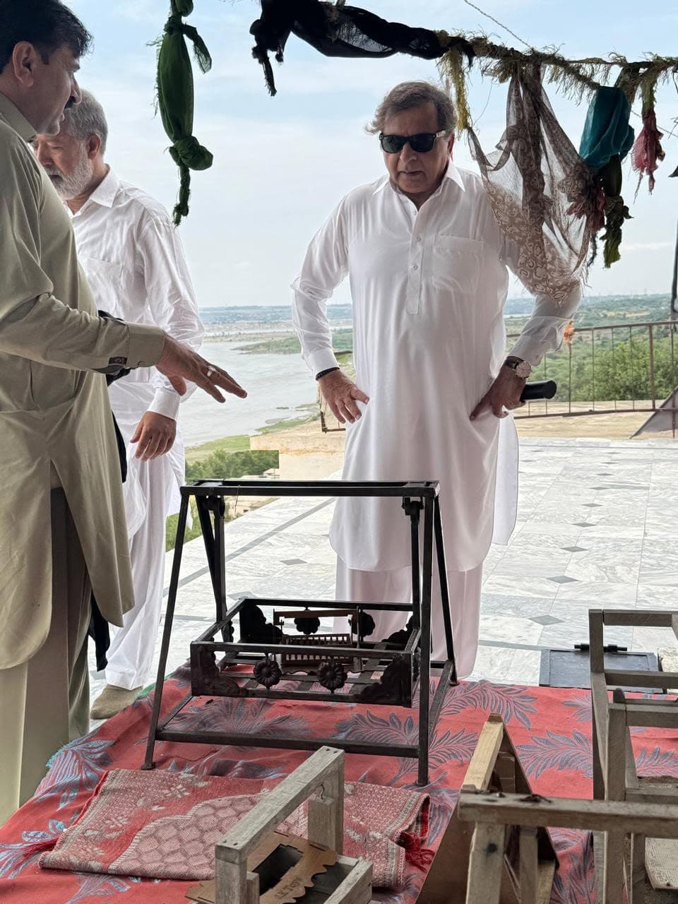 Visitors on a marble terrace hung with cloth offerings, with the Indus and plains far below