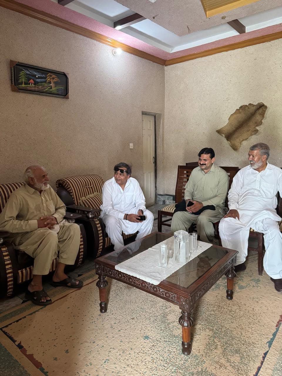 Four men in shalwar kameez talking in a sitting room with an animal skin on the wall