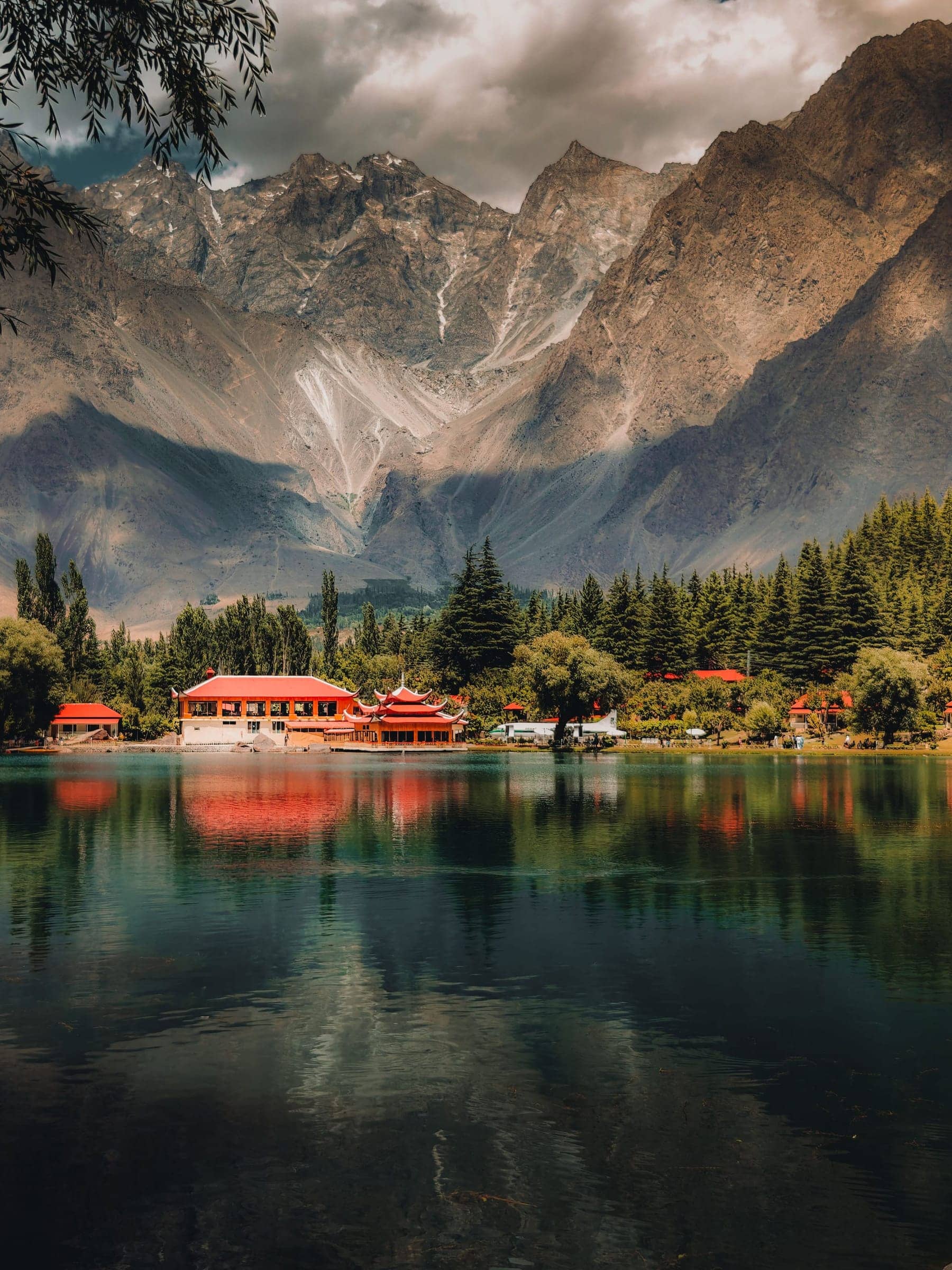 Shigar Lake with red-roofed lakeside buildings reflected below the Karakoram