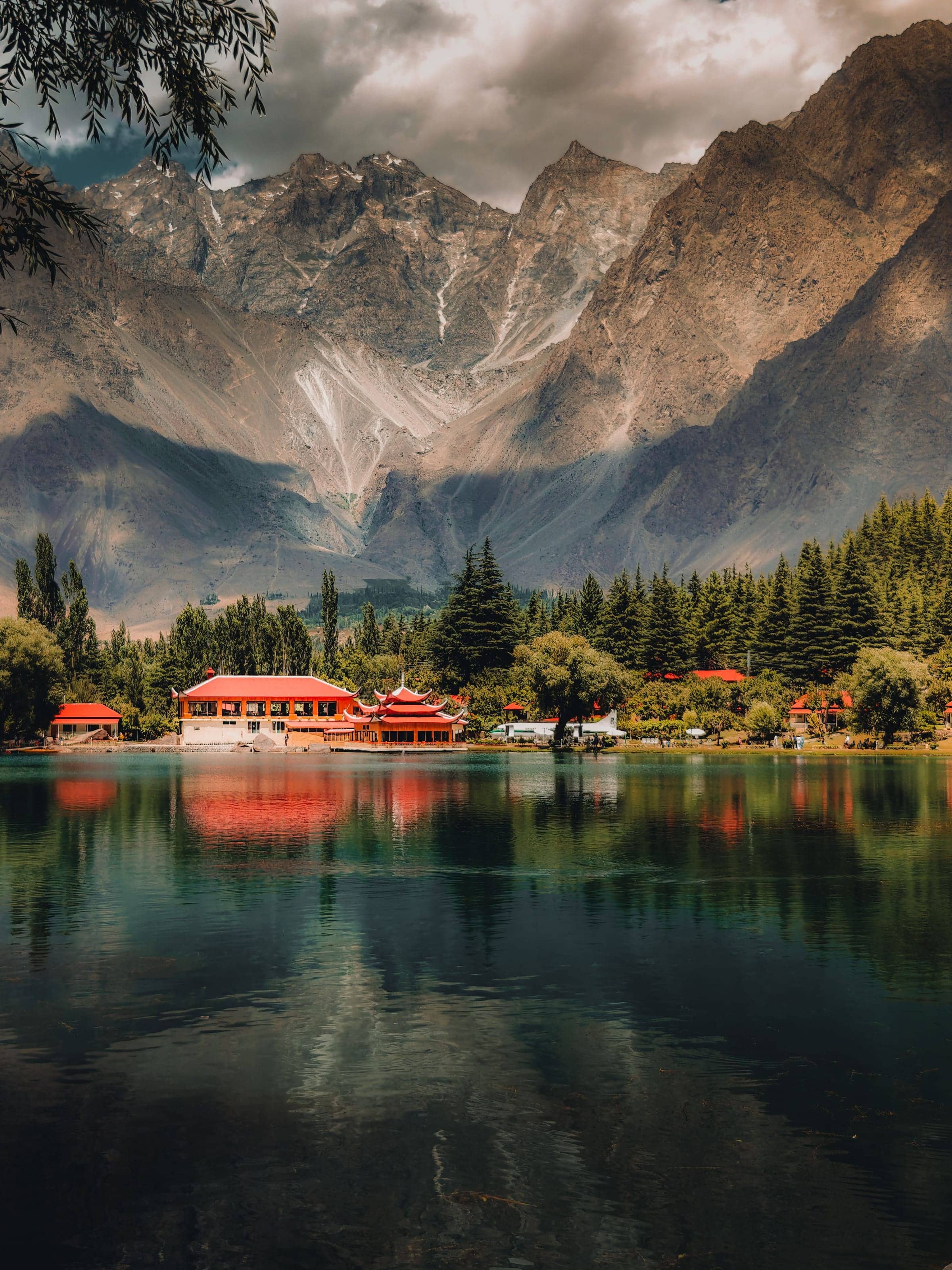 Shigar Lake with red-roofed lakeside buildings reflected below the Karakoram